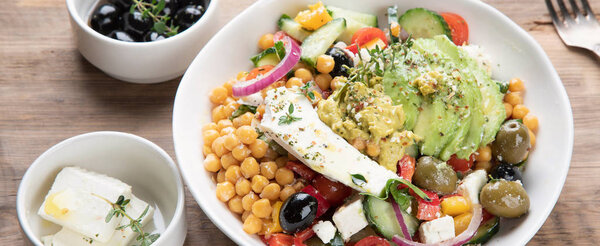 Чаша свежего салата с горохом, фета, оливки и авокадо на деревянном фоне
.