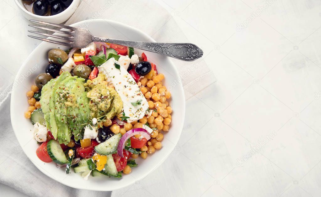 Bowl of fresh salad with chickpeas, feta, olives and avocado on table cloth.