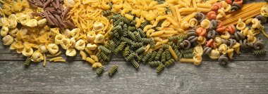 Ahşap arka planda farklı türde makarna. Diyet gıda konsepti. Kopyalama alanı olan üst görünüm. Panorama, bayrak