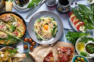 Kırsal ahşap masada iştah açıcı klasik İtalyan mutfağı. Farklı pizza, makarna, aperatif ve capreze çeşitleri. Sağlıklı ev yemekleri. Üst manzara, düz uzanma.