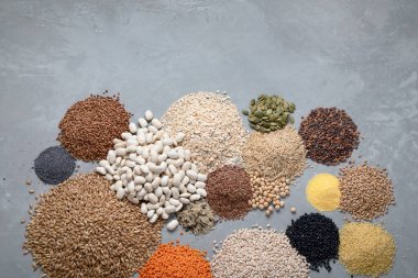 Gri arka planda çeşitli doğal tahıllar. Kopyalama alanı olan üst görünüm