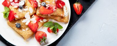 Krem şantili leziz geleneksel krepler ve gri arka planda taze çilekler. Lezzetli krepler, ince krepler. Lezzetli bir kahvaltı. Üst görünüm, pankart, telif alanı olan panorama.