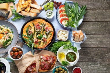 Kırsal ahşap masada iştah açıcı klasik İtalyan mutfağı. Farklı pizza, makarna, aperatif ve capreze çeşitleri. Sağlıklı ev yemekleri. Üst görünüm, telif alanı olan düz uzanma.