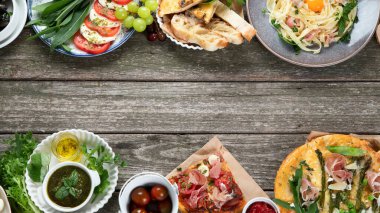 Kırsal ahşap masada iştah açıcı klasik İtalyan mutfağı. Farklı pizza, makarna, aperatif ve capreze çeşitleri. Sağlıklı ev yemekleri. Üst görünüm, kopyalama alanı olan düz uzanma.