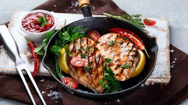 Izgara tavuk göğsü ve tavada sosla servis edilmiş gri arka planda sebzeler.. 