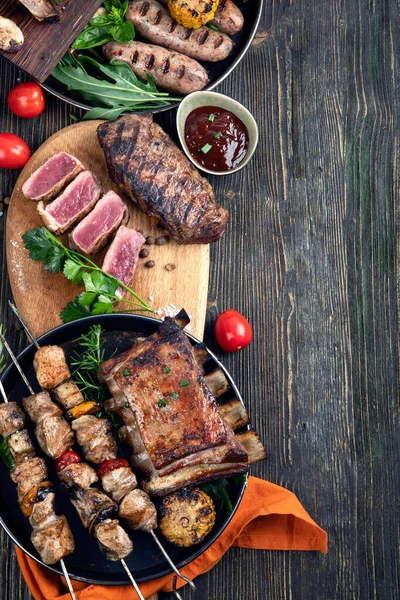 Assorted grilled meat with vegetables on wooden background. Barbecue menu. Top view, copy space.