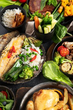 Siyah arka planda çeşitli et yemekleri, balık, salata, garnitür ve atıştırmalıklar. Üst görünüm.