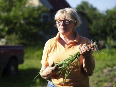Orta yaşlı beyaz bir kadın elinde genç soğan bir ürün ile