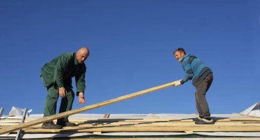 Beyaz erkekler çatı kaplama işi gerçekleştirir. Ahşap ahşap taban tahtası montajı.