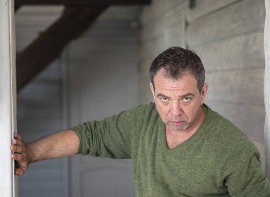 Üzgün olgun beyaz adam olarak yeşil jumper hous ahşap bir duvara sırtını yaslanmış duran