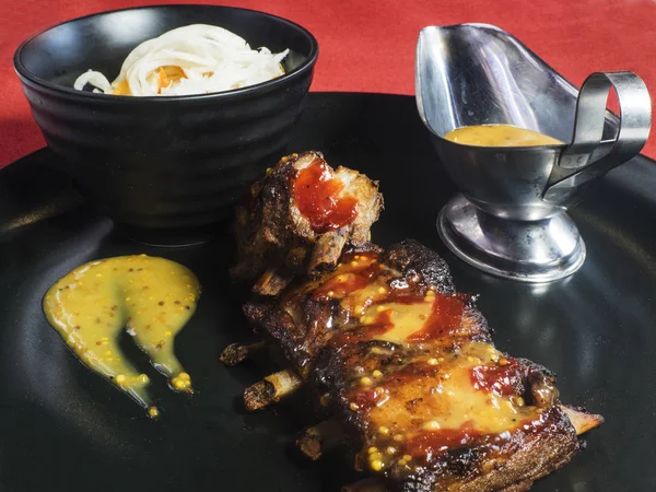 Fried pork ribs with Dijon mustard sauce and ketchup on black plat