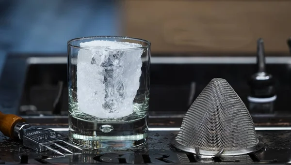 glass with a large piece of ice on the bar