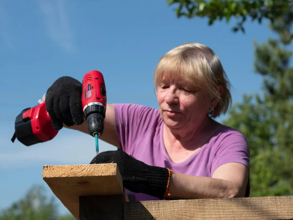 一位高个子白人妇女用螺丝刀在花园的一座农舍房顶上绑上一块木板 — 图库照片