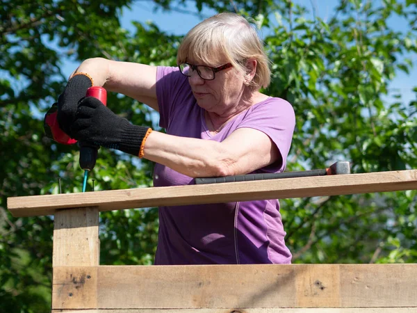 一位高个子白人妇女用螺丝刀在花园的一座农舍房顶上绑上一块木板 — 图库照片