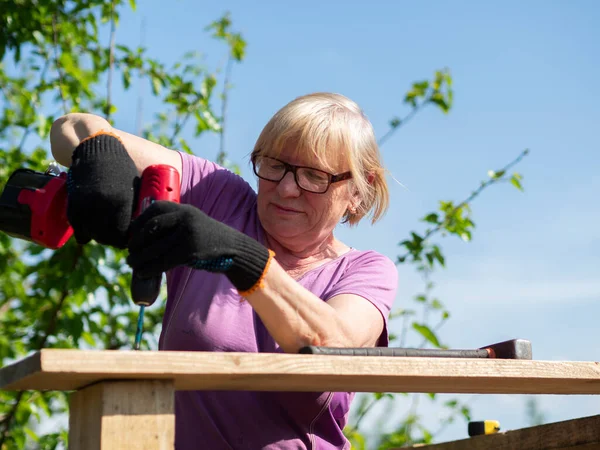 Starsza Kaukaska Kobieta Przymocowuje Deskę Dachu Budynku Gospodarskiego Ogrodzie Śrubokrętem — Zdjęcie stockowe