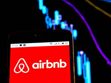 Bu fotoğraf illüstrasyonunda Airbnb logosu bir grafiğin arka planındaki eğrili akıllı bir telefonda görüntülenir. Uluslararası basında çıkan haberlere göre Coronavirus salgını sırasında COVID-2019 Airbnb 'in kurucusu 