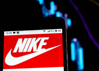 Bu resimde Nike logosu, bir grafiğin arka planında düşen eğrilerle bir akıllı telefonda görüntülenir. Uluslararası basında çıkan haberlere göre Coronavirus salgını sırasında COVID-2019 Nike 'ın toplam 23 milyar ABD doları var.