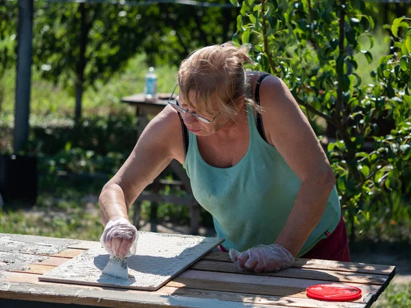 Kaukasische Senior Vrouw Installeert Keramische Tegels Tuin Houten Tafel — Stockfoto