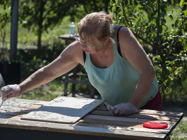 白种人老年妇女在花园木桌上安放瓷砖 — 图库照片