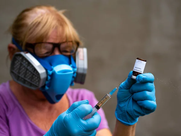 In this photo illustration with Selective focus, a scientist wearing a mediated respirator and rubber gloves syringes liquid from a vial labeled Coronavirus vaccine seen displayed as the world anxiously awaits for the vaccine against coronavirus.