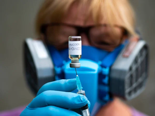 選択的焦点を当てたこの写真では 世界がコロナウイルスに対するワクチンを切望しているように見えるバイアルラベル付きコロナウイルスワクチンから仲介マスクとゴム手袋注射器を身に着けている科学者が待っています — ストック写真