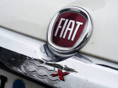 Almanya - 25 Eylül 2025: Bu fotoğraf, iki amblemli beyaz bir arabanın ön yüzünü gösteriyor. Ana olanı dairesel, kırmızı ve krom Fiat logosu. Altında, bir krom rozette kırmızı harfli 