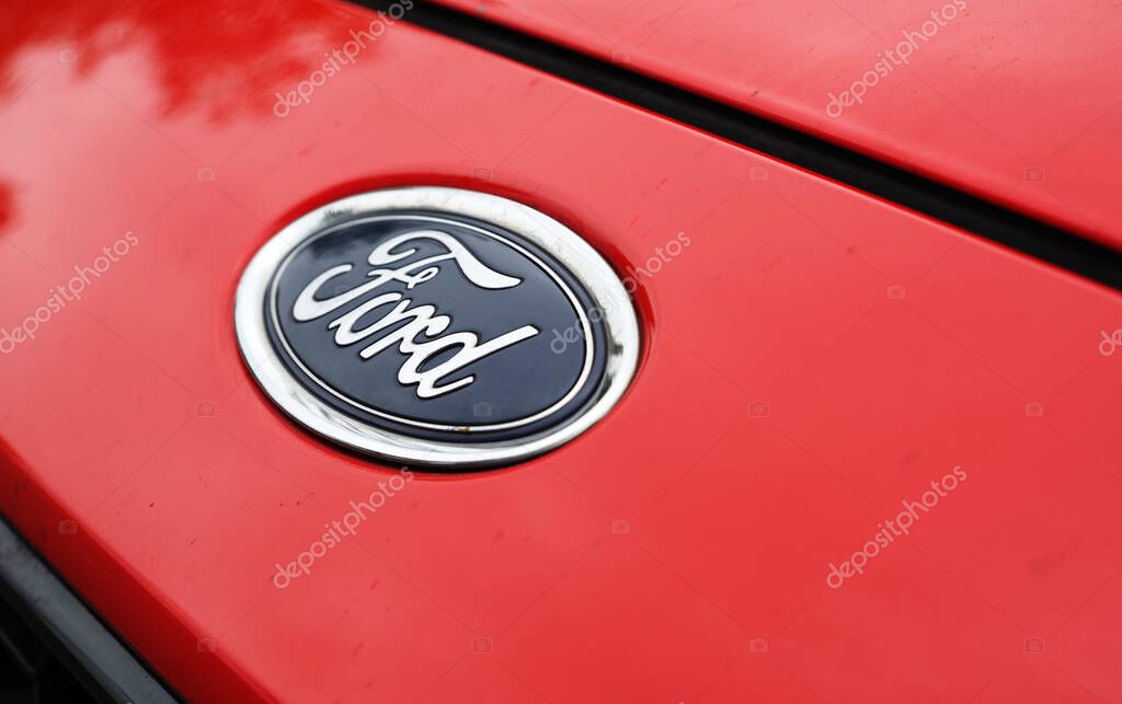 Germany - September 25, 2025: A vibrant image focusing on the classic blue oval Ford logo. The emblem is mounted on a bright red car body, creating a strong color contrast. The logo is clean and clear, and the surrounding paint is smooth and shiny. T