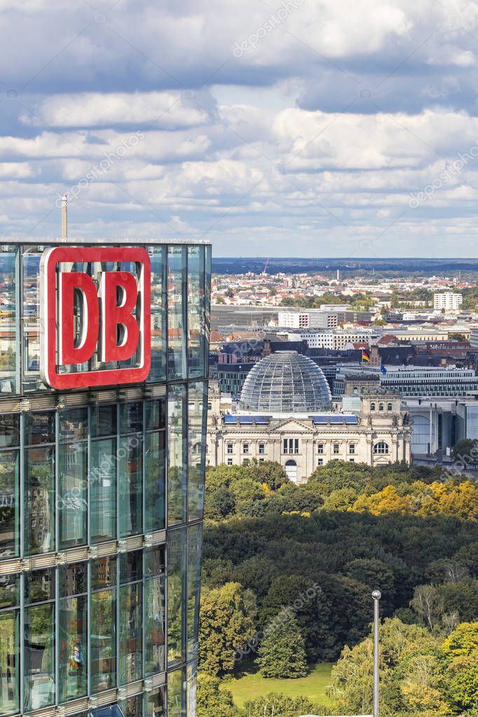 BERLIN, GERMANY - SEPTEMBER 22, 2017: DB Logo on the top of Bahn Tower, German Railway (Deutsche Bahn) HQ. German parliament building (Bundestag) on the background