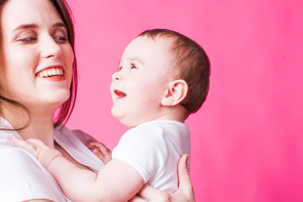 Mama fericită se uită la copilul ei zâmbitor, pe un fundal roz — Fotografie, imagine de stoc