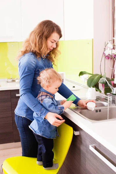 Bulaşıkları yıkama bir oğlan çocuğu ile Genç Anne