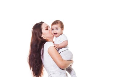 Güzel genç Anne kucağında çocuğunu tutan ve beyaz bir arka plan üzerinde beyaz bezler, giyen bebeği öper