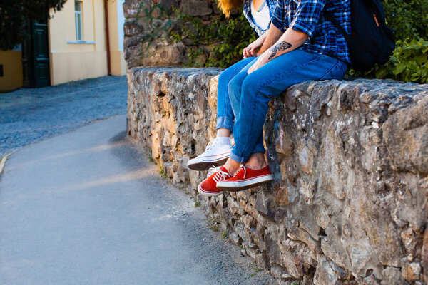 Фото туловища с ногами молодой пары, одетой в современную одежду и сидящей на каменной стене
