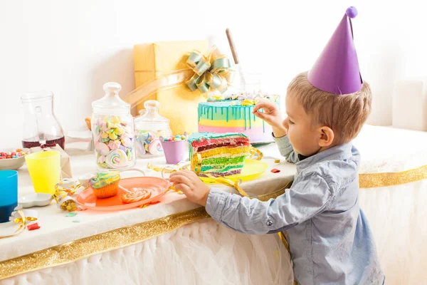 O menino com chapéu de aniversário quer experimentar este bolo saboroso — Fotografia de Stock