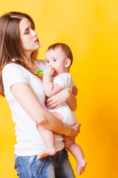 Jovem mãe segurando seu filho, isolada em fundo amarelo — Fotografia de Stock