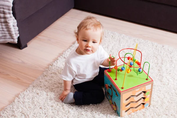Маленький мальчик сидит на мягком ковре с игрушкой в руках — стоковое фото