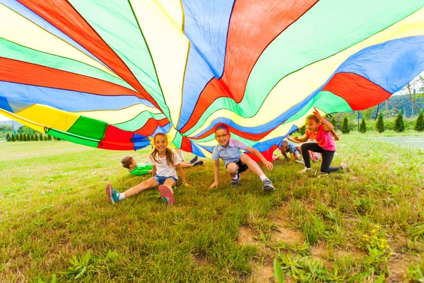 Sonriente chico y chica bajo colorido paracaídas — Foto de Stock