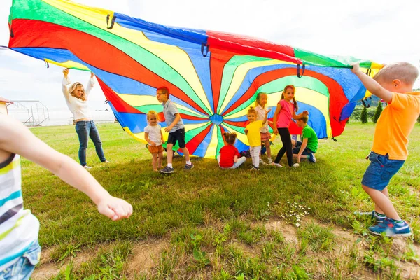 Gelukkige jonge geitjes zwaaien regenboog parachute — Stockfoto