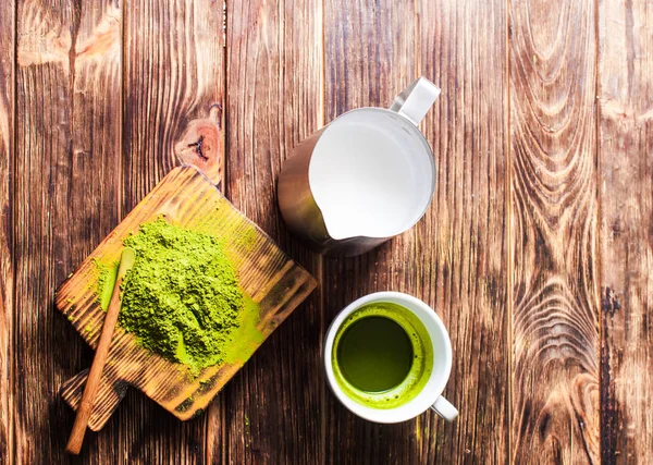 Una taza de té Matcha con jarra de leche y té verde en polvo en la mesa de madera . — Foto de Stock