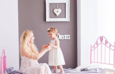 Mutlu anne ve kızı beyaz elbiseler yatakta bir buket çiçek yanında oturan