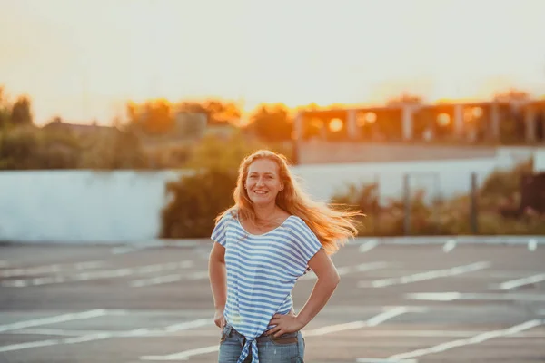 Mulher sorridente de pé nos raios do sol da noite — Fotografia de Stock