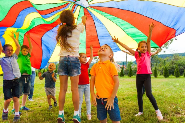 Niños alegres rebotando bajo el dosel del arco iris textil —  Fotos de Stock