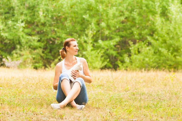 Atrakcyjna kobieta siedzi na trawie z kotem na kolanach — Zdjęcie stockowe