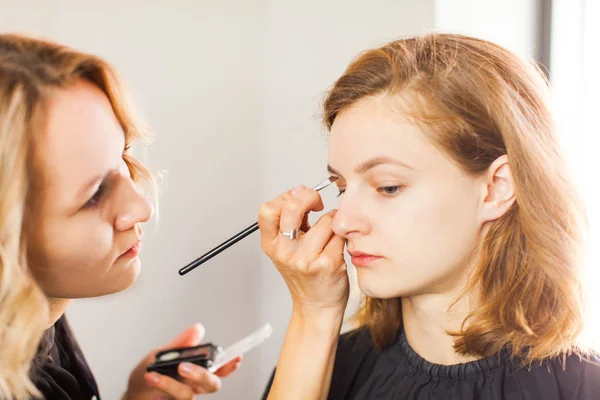 Estilista hace joven chica profesional maquillaje — Foto de Stock