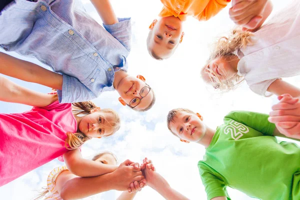 Blick von unten auf eine Gruppe glücklicher Schulkinder, die im Kreis stehen — Stockfoto