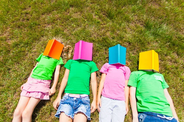 Quatro crianças deitadas num chão com livros na cara — Fotografia de Stock