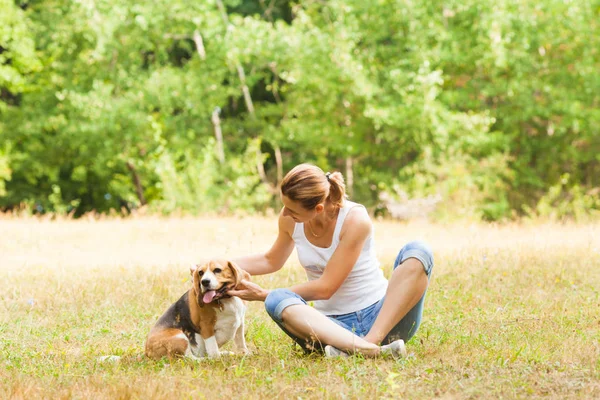 屋外の芝生の上に座っている彼女の犬をかわいがる女性 — ストック写真