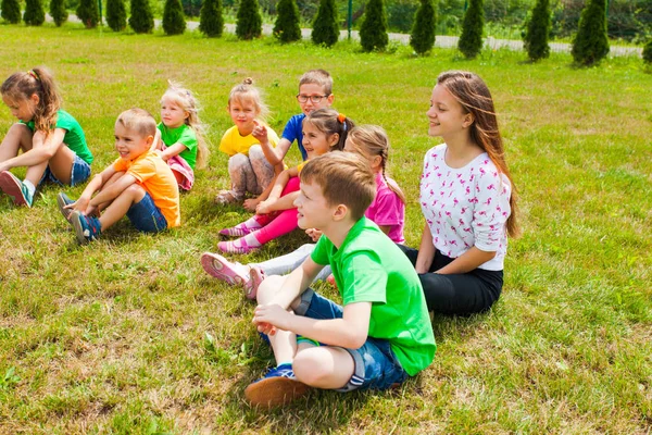 Niños sonrientes sentados en una hierba en una lección al aire libre — Foto de Stock