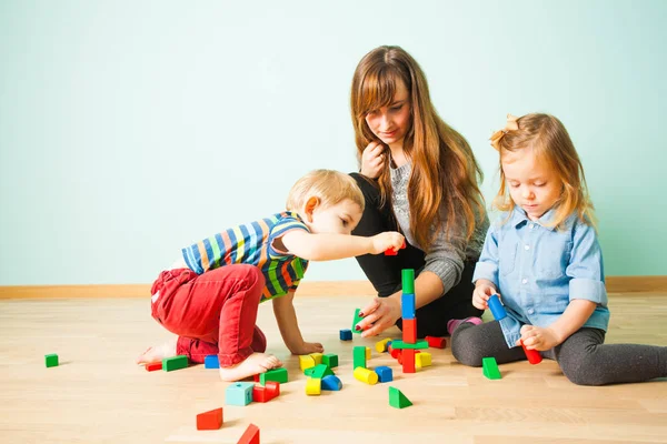 Annesi ona yardım çocuklar renkli bloklardan inşa. — Stok fotoğraf