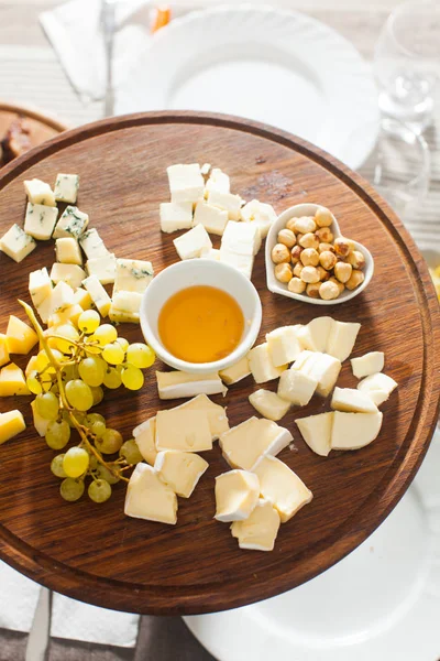Käseteller mit Haselnüssen, Honig, Trauben auf Holztisch — Stockfoto