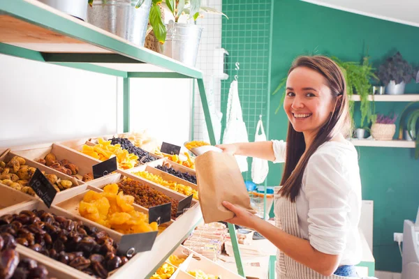 Mujer joven vendedor paquetes de frutas secas en la tienda de comestibles —  Fotos de Stock